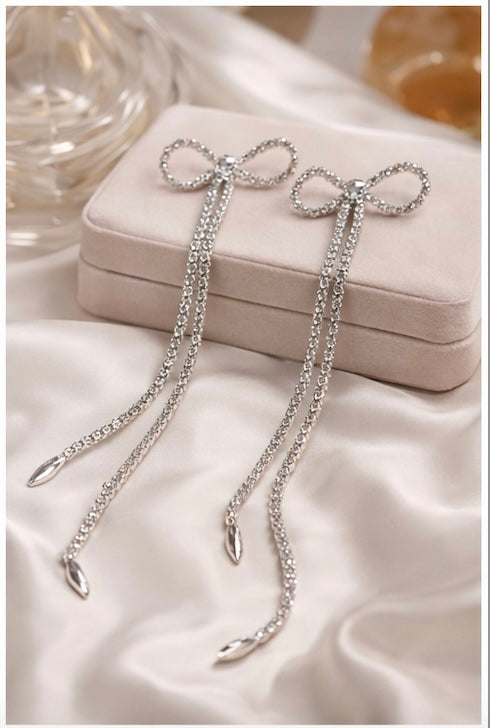 Silver bow-shaped earrings with chains on a white satin surface