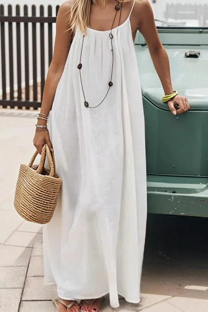 Woman in a white dress holding a straw bag, standing next to a vintage car.