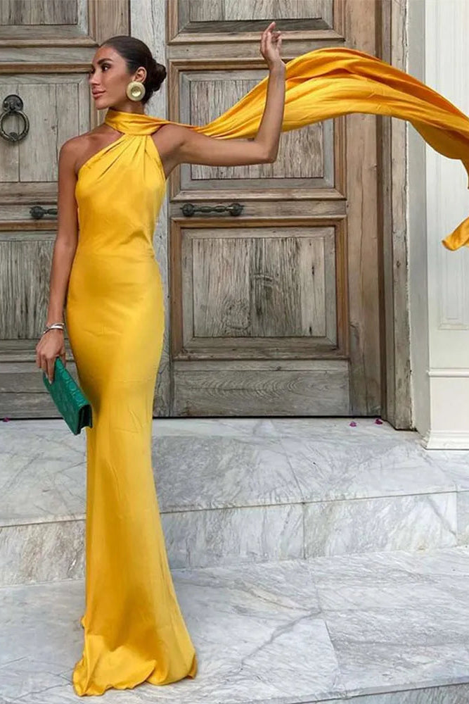 Woman in a yellow evening gown holding a flowing fabric against a marble floor and wooden door background.