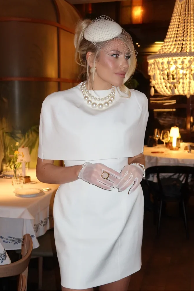 Woman in a white dress with gloves and pearls in a restaurant setting