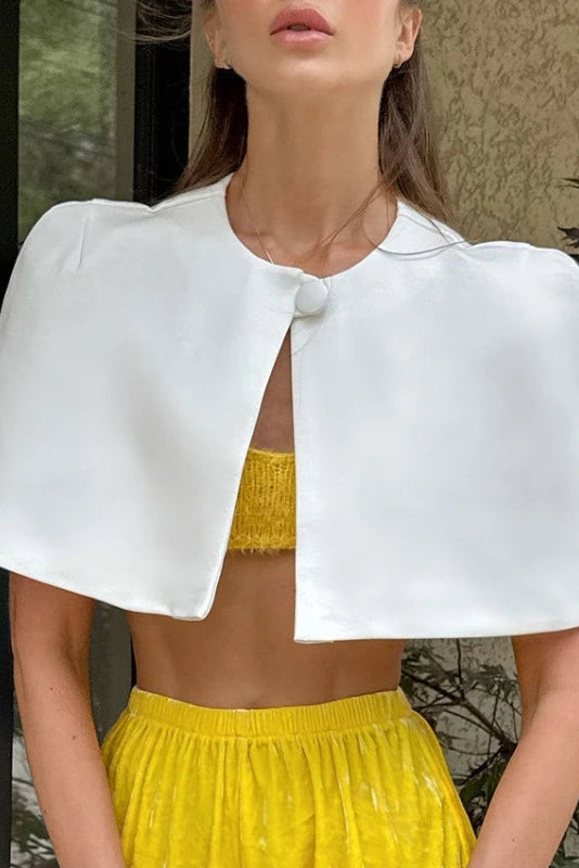 Woman wearing a white cape over a yellow top and skirt outdoors.