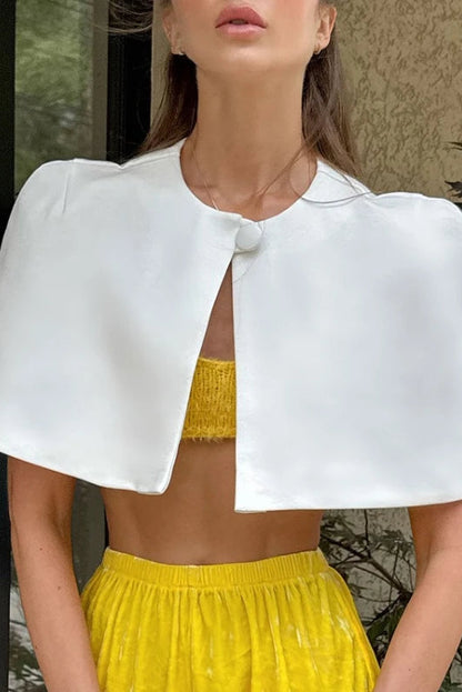 Woman wearing a white cape over a yellow top and skirt outdoors.