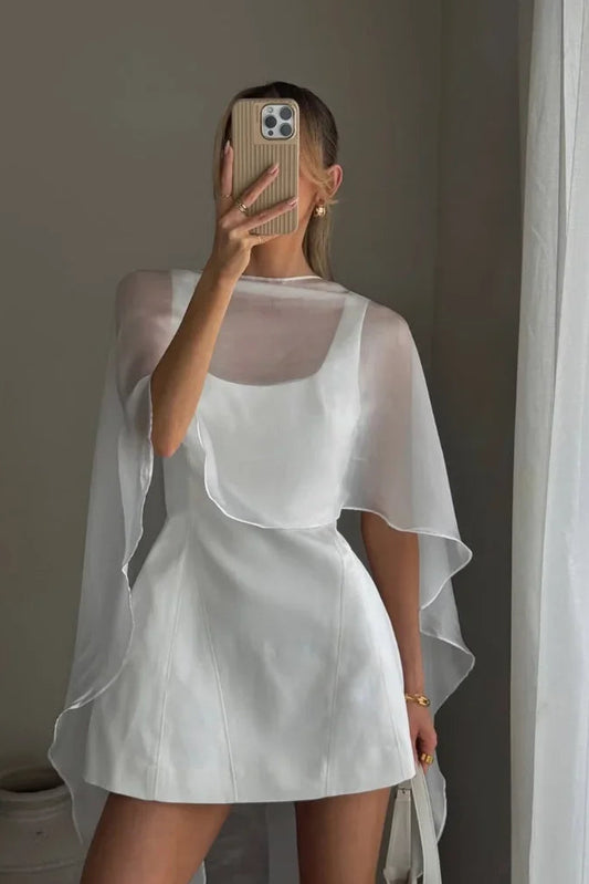 Person wearing a white dress with a sheer overlay in a minimal indoor setting.