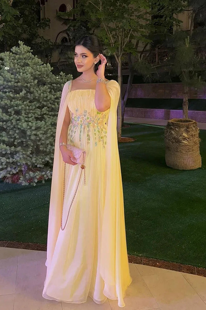 Woman in a yellow dress standing outdoors with greenery in the background