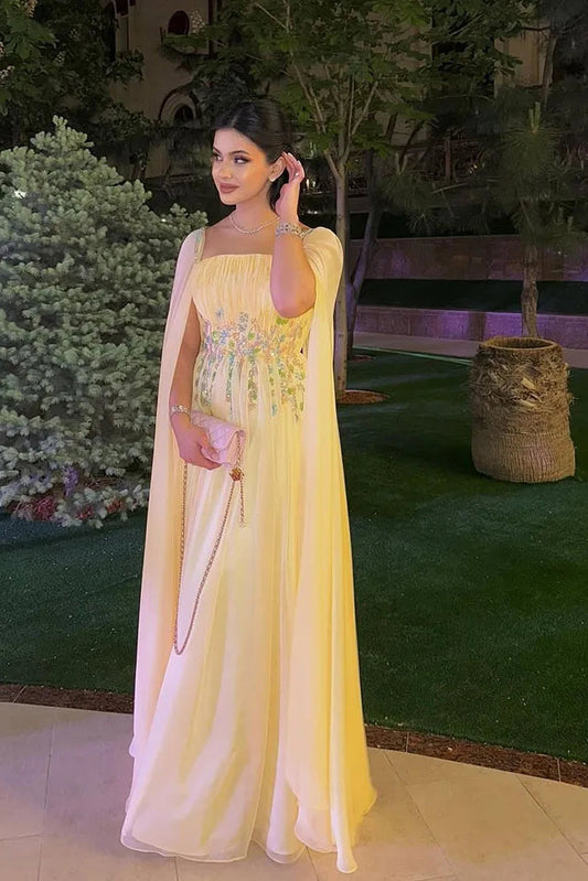 Woman in a yellow dress standing outdoors with greenery in the background