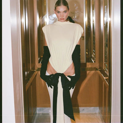 Woman wearing a white dress with a high slit and black gloves in a reflective room.