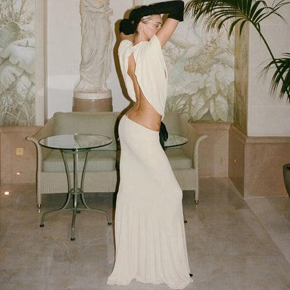 Woman in a white dress standing in an elegant room with a statue and table in the background.